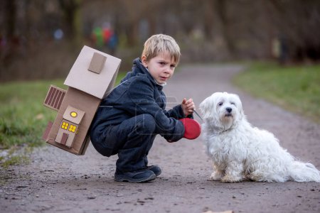 Foto de Little child, blond boy with pet dog, carying home on his back, kid, having paper house, emotional shot - Imagen libre de derechos