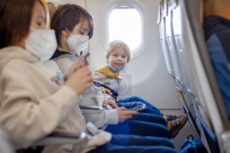 Photo for Mother and child, boy and mom, sitting in airplane, child playing on tablet, family trip - Royalty Free Image