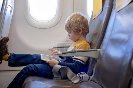 Téléchargez les photos : Mère et enfant, garçon et maman, assis dans l'avion, enfant jouant sur tablette, voyage en famille - en image libre de droit