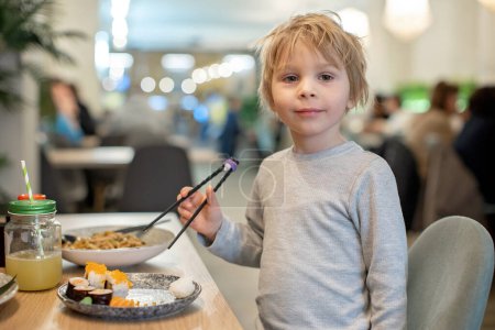 Téléchargez les photos : Enfant, manger des sushis japonais et des nouilles avec des baguettes dans un restaurant, dîner - en image libre de droit
