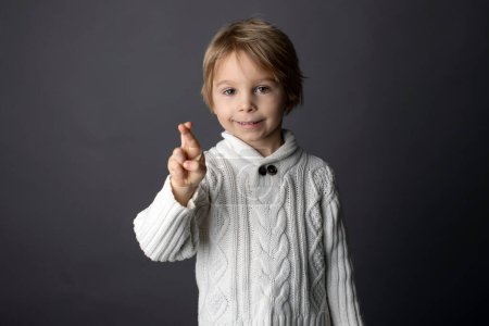 Téléchargez les photos : Cute little toddler boy, showing FINGER CROSSED gesture in sign language on gray background, isolated image, child showing hand sings for deaf people - en image libre de droit