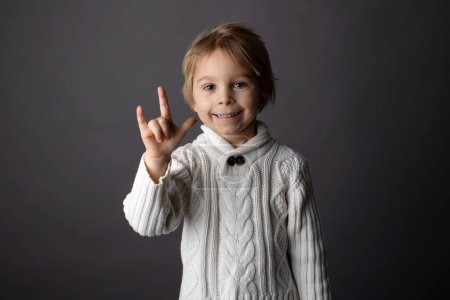 Téléchargez les photos : Mignon petit garçon tout-petit, montrant JE VOUS AIME geste en langue des signes sur fond gris, image isolée, enfant montrant la main chante pour les personnes sourdes - en image libre de droit