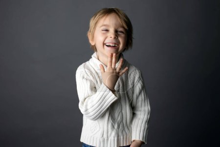 Netter kleiner Junge, zeigt DANKE Geste in Gebärdensprache auf grauem Hintergrund, isoliertes Bild, Kind zeigt Handgesang für Gehörlose
