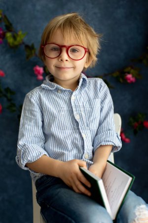 Photo for Cozy spring atmosphere at home, child sitting on chair reading a book, wearing glasses, enjoying - Royalty Free Image