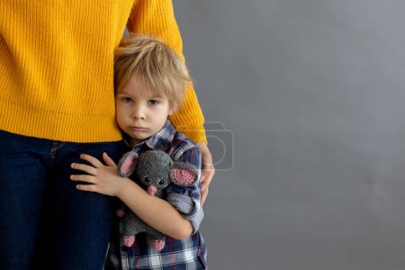 Photo for Sad little child, blond boy, hugging his mother at home, holding teddy bear - Royalty Free Image