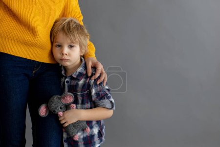 Photo for Sad little child, blond boy, hugging his mother at home, holding teddy bear - Royalty Free Image