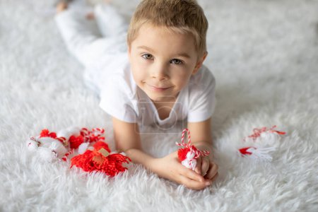 Foto de Lindo niño, niño rubio, jugando con brazalete blanco y rojo, martenitsa bulgara - Imagen libre de derechos