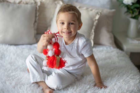Niedliches Kind, blonder Junge, spielt mit weißem und rotem Armband, bulgarische martenitsa