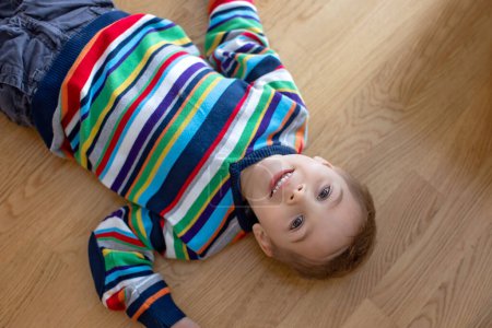 Téléchargez les photos : Cute child, blond boy, lying on the floor at home, looking at camera, shot from above - en image libre de droit