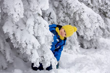 Téléchargez les photos : Doux enfant heureux, jouant dans la neige profonde dans la forêt - en image libre de droit