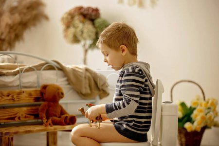 Foto de Lindo niño pequeño, muchacho, usando el orinal en casa, mientras que juega con los juguetes, entrenamiento del orinal - Imagen libre de derechos