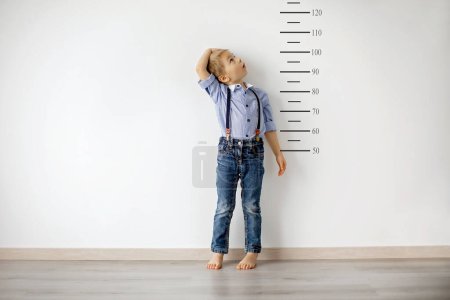 Photo for Little child, blond boy, measuring height against wall in room - Royalty Free Image