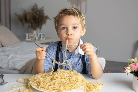 Photo for Cute preschool child, blond boy, eating spaghetti at home, making a mess everywhere, funny moments - Royalty Free Image