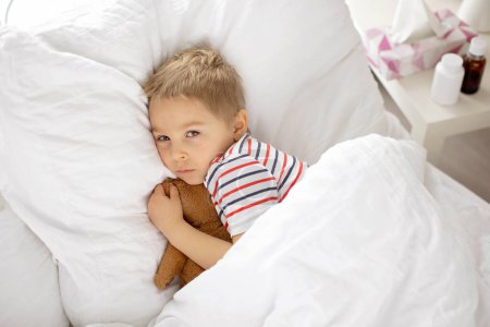 Foto de Dulce niño rubio preescolar con oso de peluche, acostado en la cama enfermo, dormitorio soleado - Imagen libre de derechos