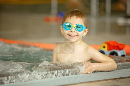 Photo for Child, taking swimming lessons in a group of children in indoor pool, enjoying learning - Royalty Free Image