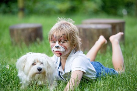 Foto de Pequeño bebé niño, niño con la cara pintada como un perro, jugando con el perro mascota en el jardín en la fiesta de cumpleaños - Imagen libre de derechos