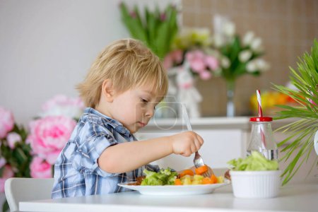 Foto de Niño pequeño, niño rubio, comer verduras hervidas, brócoli, papas y zanahorias con carne de pollo frito en casa, comida sana casera recién cocinada - Imagen libre de derechos