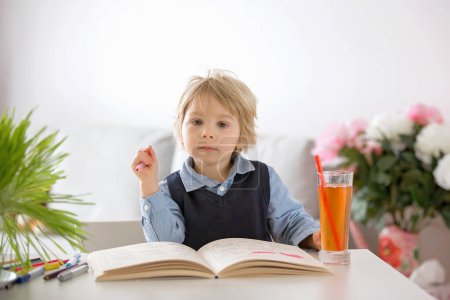 Photo for Cute preschool child, blond boy, filling some homework in a book and coloring pictures - Royalty Free Image