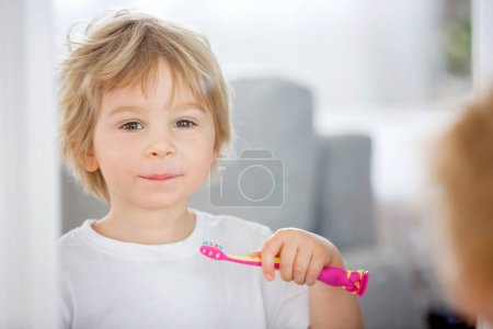 Foto de Lindo niño, rubio, cepillándose los dientes en casa, aislado - Imagen libre de derechos