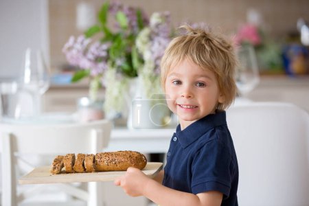 Téléchargez les photos : Enfant, jeune garçon blond, tenant une planche à découper en bois avec du pain de maïs fait maison, servant à la maison du pain frais - en image libre de droit