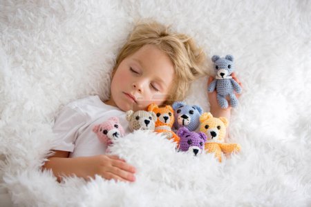 Photo for Little toddler child, cute blond boy, sleeping with many teddy bears, handmade amigurumi toys at home in bed - Royalty Free Image