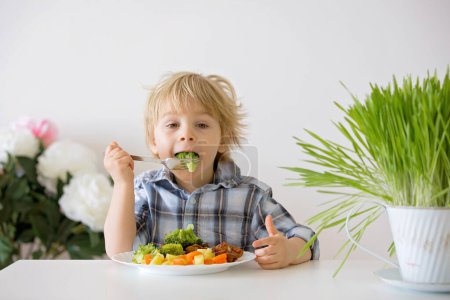 Photo for Little toddler child, blond boy, eating boiled vegetables, broccoli, potatoes and carrots with fried chicken meat at home, homemade freshly cooked healthy food - Royalty Free Image