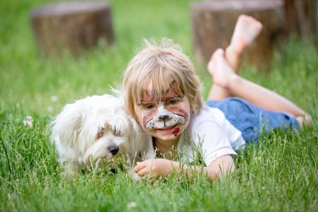 Photo for Little toddler baby boy, child with painted face as a dog, playing with pet dog in the garden on birthday party - Royalty Free Image