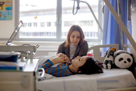 Téléchargez les photos : Enfant préadolescent, garçon, allongé à l'hôpital avec fracture de la colonne thoracique, vertèbres, mère assise à côté de son lit - en image libre de droit