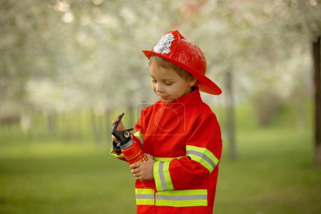 Foto de Little toddler child with fireman costume in park, pretending to be real fireman, playing on sunset - Imagen libre de derechos