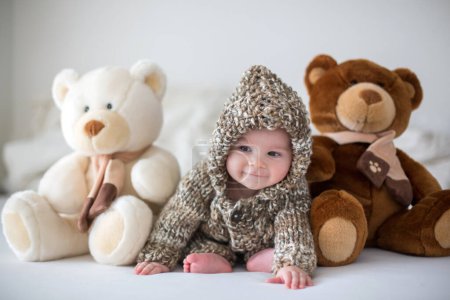 Photo for Little baby boy playing at home with soft teddy bear toys, sitting in bed - Royalty Free Image