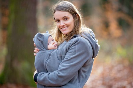 Téléchargez les photos : Mère, portant son petit garçon dans une fronde, en plein air heure d'hiver - en image libre de droit