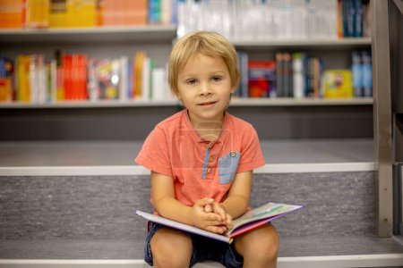 Photo for Cute preschool child, sitting in a bookstore, looking at books on summer day - Royalty Free Image
