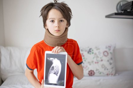 Téléchargez les photos : Enfant préadolescent, garçon, tenant un comprimé avec une image de colonne vertébrale thoracique fracturée, portant un fixateur de col mou - en image libre de droit