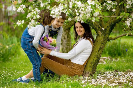 Téléchargez les photos : Young pregnant woman, receiving bouquet of colorful flowers from her children for Mothers Day, sitting in a beautiful spring blooming garden - en image libre de droit