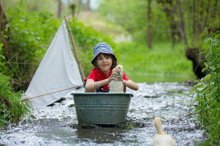 Téléchargez les photos : Enfant mignon, garçon, jouer avec le bateau et les canards sur une petite rivière, voile et canotage. Enfant s'amuser, concept de bonheur d'enfance - en image libre de droit