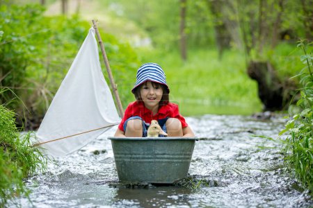Foto de Niño lindo, niño, jugando con barco y patos en un pequeño río, vela y paseos en bote. Niño divertirse, concepto de felicidad de la infancia - Imagen libre de derechos