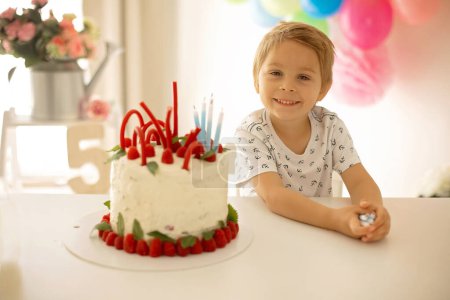 Foto de Lindo niño, niño preescolar, celebrando cumpleaños en casa con pastel casero con frambuesas, menta y caramelos, globos y decoración en la habitación - Imagen libre de derechos