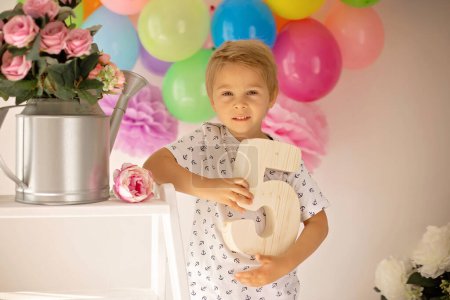 Foto de Lindo niño, niño preescolar, celebrando cumpleaños en casa con pastel casero con frambuesas, menta y caramelos, globos y decoración en la habitación - Imagen libre de derechos