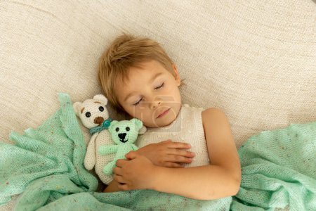 Photo for Little toddler child, cute kid with knitted small cute animal toy, lying in bed, cuddling - Royalty Free Image