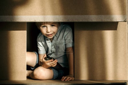Photo for Cute toddler child and maltese pet dog, hiding in cardboard box, playing together - Royalty Free Image