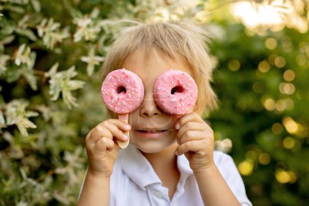 Téléchargez les photos : Cute child, boy, eating doughnut ice cream in the backyard of his home garden, summertime - en image libre de droit