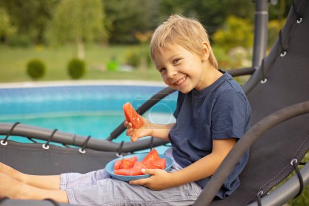 Photo for Cute child, boy, eating watermelon in garden, next to a pool, swinging - Royalty Free Image