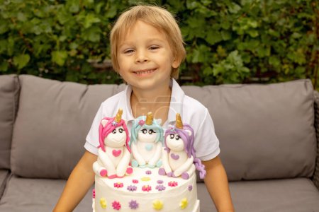 Téléchargez les photos : Cute five years old child, sitting in garden with big homemade cake with unicorns, celebrating birthday, beautifully decorated cake - en image libre de droit