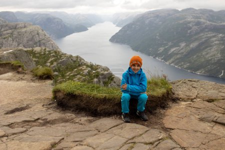 Photo for Family, enjoying the hike to Preikestolen, the Pulpit Rock in Lysebotn, Norway on a rainy day, toddler climbing with his pet dog the one of the most scenic fjords in Norway - Royalty Free Image