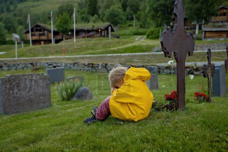 Photo for Sad little child, blond boy, standing in the rain on cemetery, sad person, mourning - Royalty Free Image