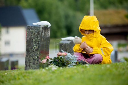 Téléchargez les photos : Sad little child, blond boy, standing in the rain on cemetery, sad person, mourning - en image libre de droit
