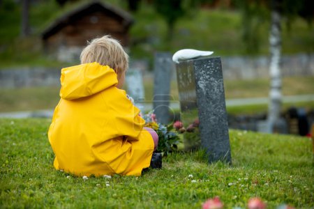 Foto de Sad little child, blond boy, standing in the rain on cemetery, sad person, mourning - Imagen libre de derechos