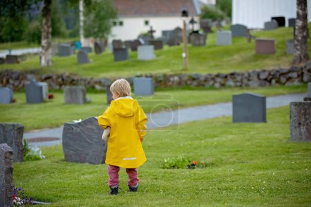 Téléchargez les photos : Sad little child, blond boy, standing in the rain on cemetery, sad person, mourning - en image libre de droit