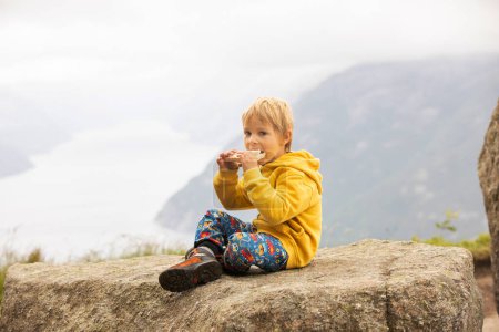 Téléchargez les photos : Family, enjoying the hike to Preikestolen, the Pulpit Rock in Lysebotn, Norway on a rainy day, toddler climbing with his pet dog the one of the most scenic fjords in Norway - en image libre de droit