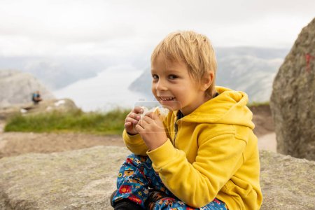 Foto de Family, enjoying the hike to Preikestolen, the Pulpit Rock in Lysebotn, Norway on a rainy day, toddler climbing with his pet dog the one of the most scenic fjords in Norway - Imagen libre de derechos